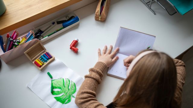 A young girl does homework at a desk with an asthma inhaler close by. Asthma is a lifelong health condition, and school is an opportunity for a child to take steps toward managing asthma on their own. 