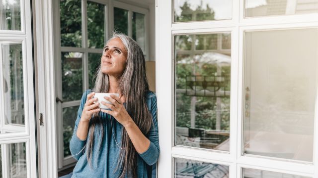 A middle-aged woman drinks coffee on an enclosed porch in the morning. For caregivers of people with Parkinson's disease, taking time to relax can prevent caregiver burnout.