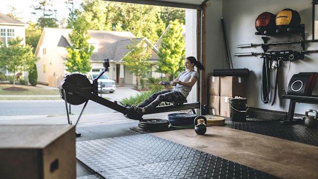 A woman uses a rowing machine in a home gym set up in her garage.