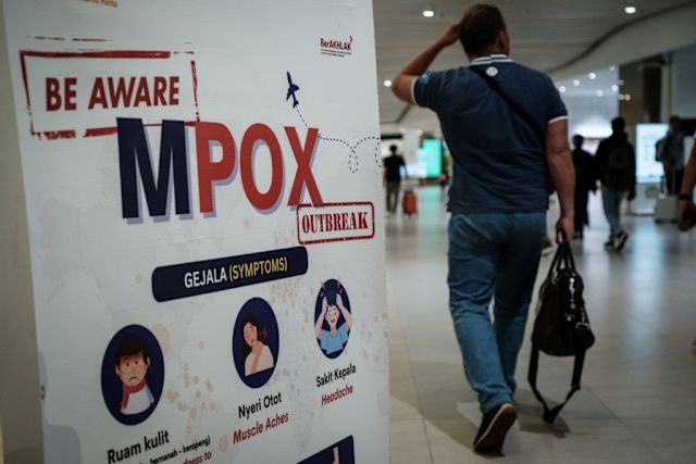 man walking in airport next to an mpox awareness and warning sign