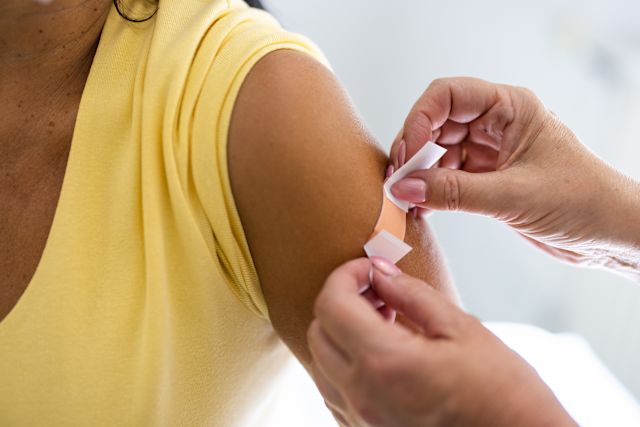 closeup shot of a woman with dark skin wearing a yellow sleeveless t-shirt getting vaccinated with a COVID-19 vaccine