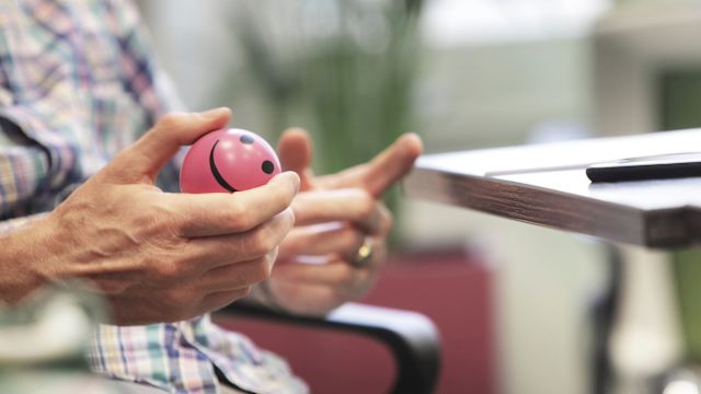 A senior man squeezes a stress ball to relax as his ophthalmologist talks through the steps for an anti-VEGF injection.