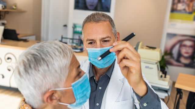 An eye care provider examines the eyes of a senior woman with a flashlight during an appointment to discuss vision changes.