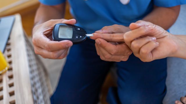 A healthcare provider tests a patient's blood glucose levels with a blood glucose meter. Elevated blood glucose levels and/or type 2 diabetes are risk factors for fatty liver disease.