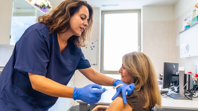 A middle-aged woman receives a flu shot in her arm at her healthcare provider's office.