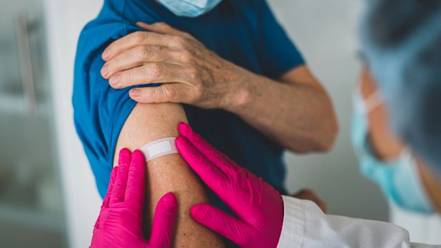 A healthcare provider applies a brightly colored adhesive bandage onto the arm of a patient who has just received his annual flu vaccine.