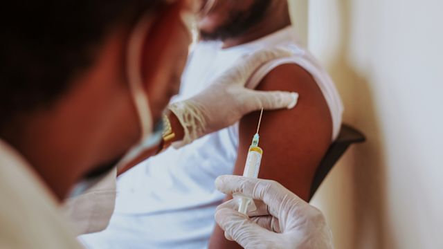 A healthcare provider administers a flu shot into the upper arm of a male patient during a healthcare appointment.