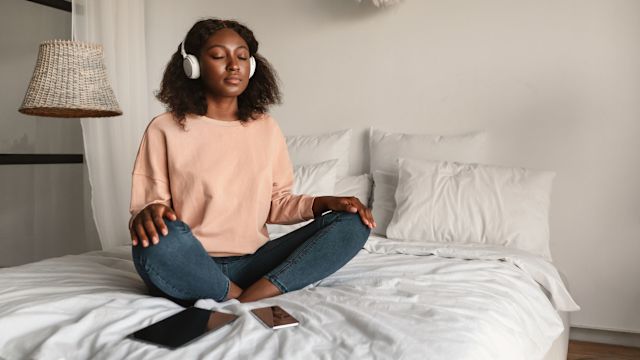 Young woman sits on bed listening to music. 