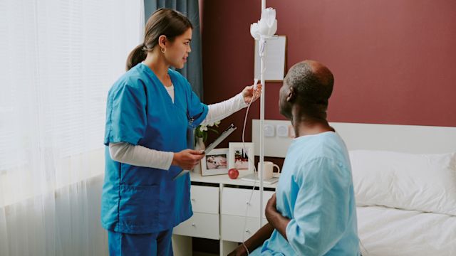 A male cancer patient with multiple myeloma talks to his infusion specialist in a hospital room prior to chemotherapy to prepare for CAR T-cell therapy.