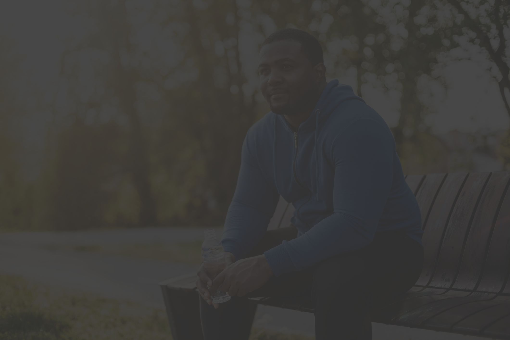 a fit but overweight Black man sits on a park bench after exercising