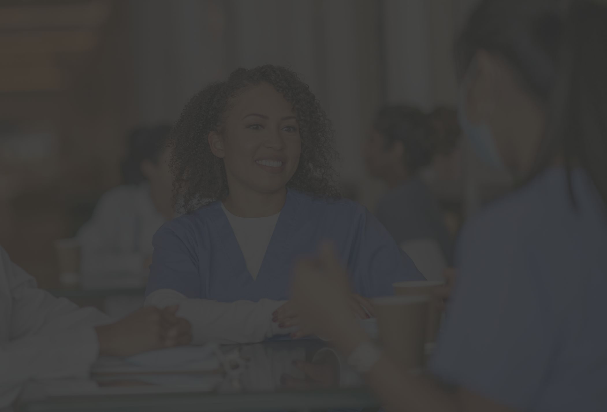 several nurses sit around a table at the cafeteria during lunch enjoying a conversation