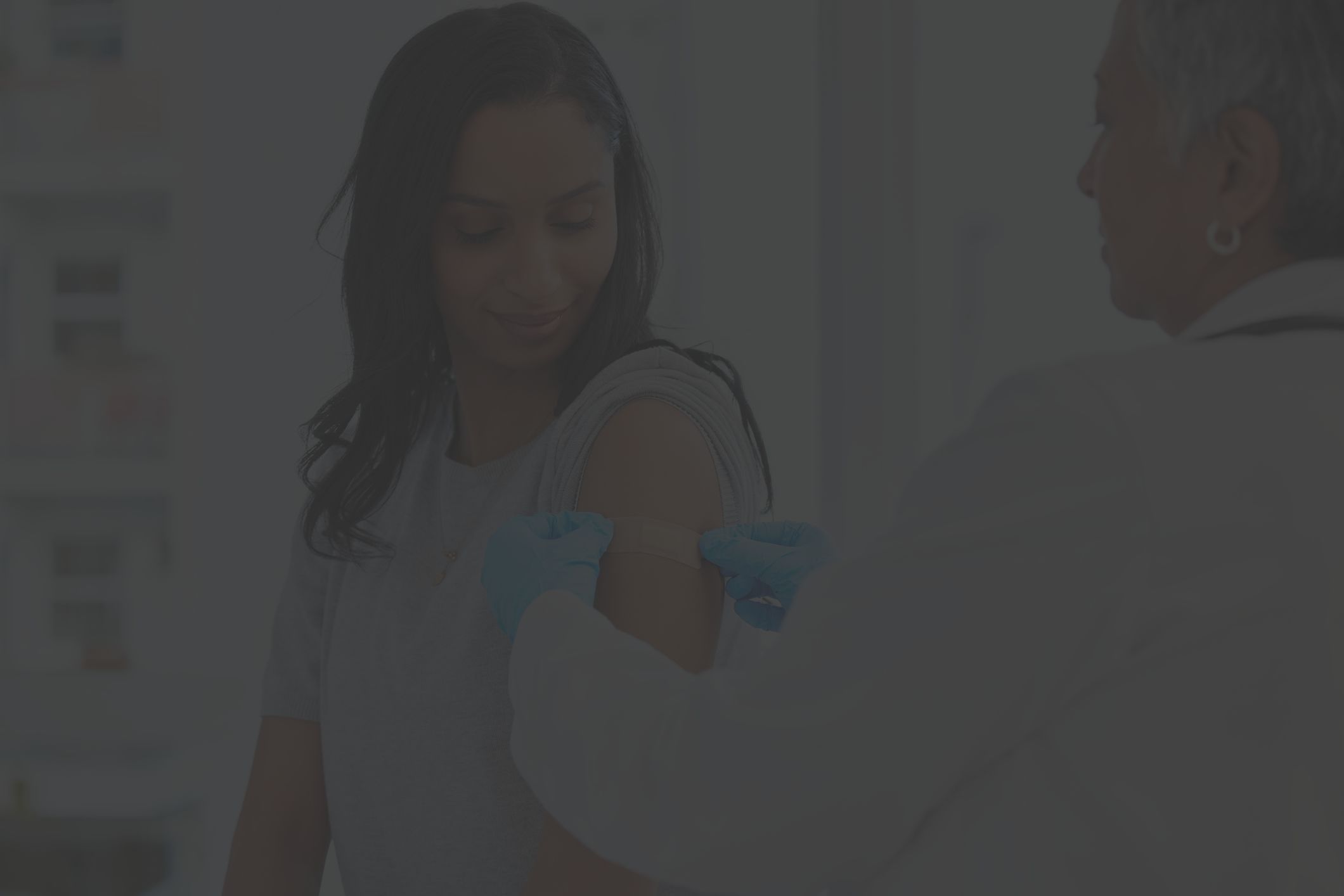 a young Black woman receives a bandage from her healthcare provider after receiving a vaccination