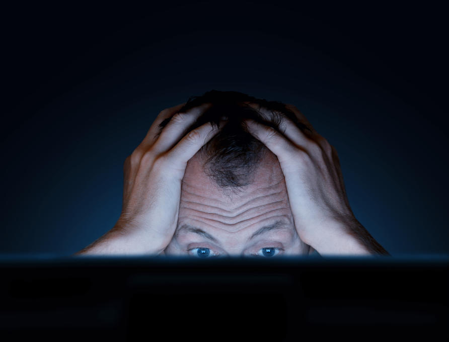 Man looking at computer screen with hands on this head in frustration