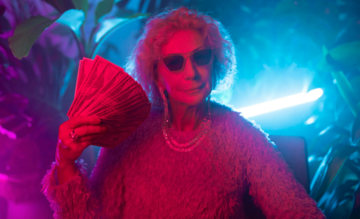 An older woman in sunglasses and sweater fanning herself with a stack of money.
