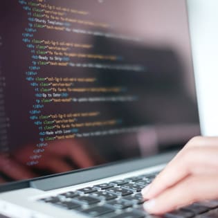 A person typing on a laptop with HTML code visible on the screen.