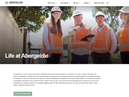 Four construction workers in hard hats and safety vests, two men and two women, stand outdoors.